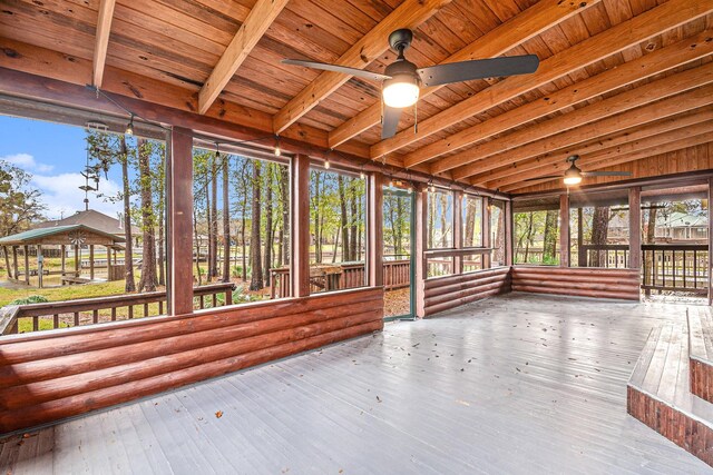 unfurnished sunroom featuring ceiling fan, plenty of natural light, beamed ceiling, and wooden ceiling