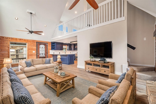 living room featuring wooden walls, ceiling fan, light hardwood / wood-style floors, and high vaulted ceiling