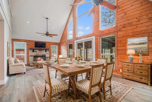 dining room with wood walls, high vaulted ceiling, light wood-type flooring, a fireplace, and a healthy amount of sunlight