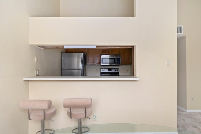 kitchen with light carpet, a kitchen breakfast bar, stainless steel appliances, and kitchen peninsula