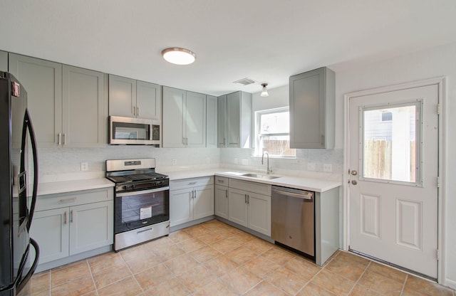 kitchen with gray cabinetry, sink, decorative backsplash, light tile patterned floors, and appliances with stainless steel finishes