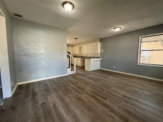 unfurnished living room featuring dark hardwood / wood-style floors, sink, and a textured ceiling