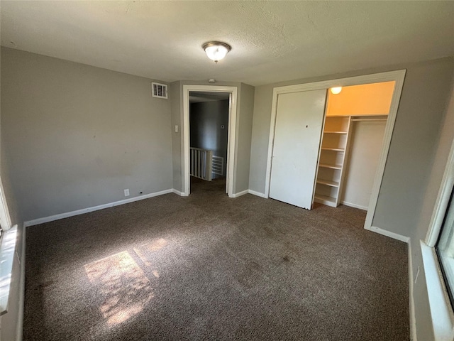 unfurnished bedroom with dark carpet, a walk in closet, a textured ceiling, and a closet