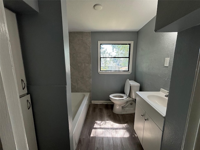 bathroom with a tub to relax in, vanity, wood-type flooring, and toilet