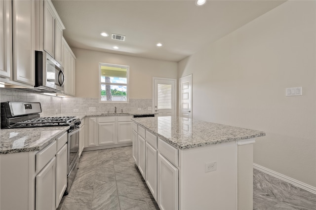 kitchen with a center island, white cabinets, sink, light stone counters, and stainless steel appliances