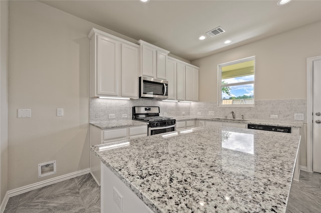 kitchen with white cabinets, sink, appliances with stainless steel finishes, a kitchen island, and light stone counters