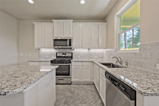 kitchen with white cabinets, appliances with stainless steel finishes, light stone countertops, and sink