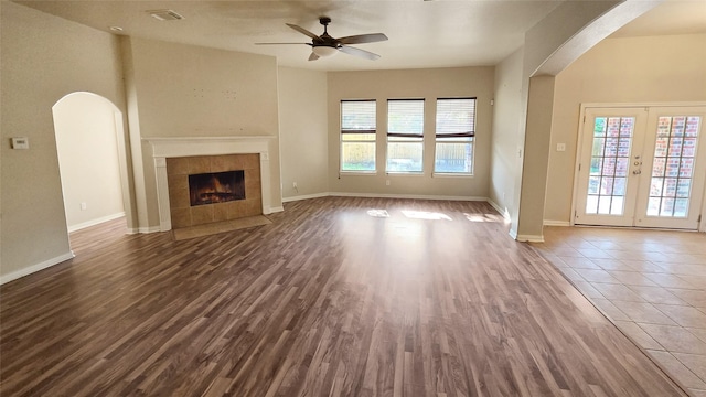 unfurnished living room with a tile fireplace, ceiling fan, french doors, and wood-type flooring