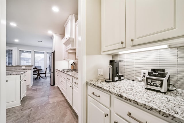 kitchen with light stone countertops, backsplash, premium range hood, white cabinets, and appliances with stainless steel finishes