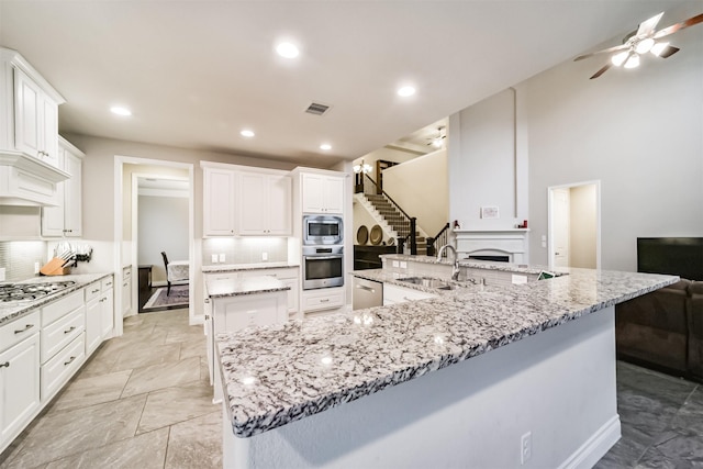 kitchen with white cabinetry, sink, stainless steel appliances, tasteful backsplash, and a large island with sink