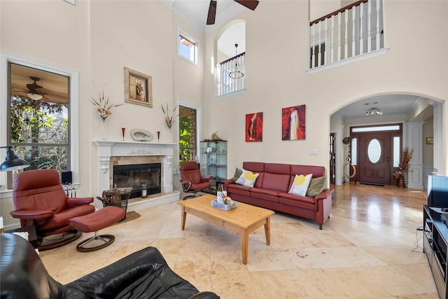 living room with a fireplace, a high ceiling, ceiling fan, and ornamental molding