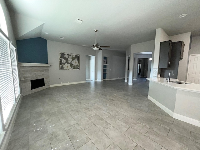 unfurnished living room featuring sink, ceiling fan, a healthy amount of sunlight, and a tiled fireplace