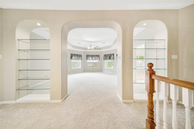 hallway with light carpet and a tray ceiling