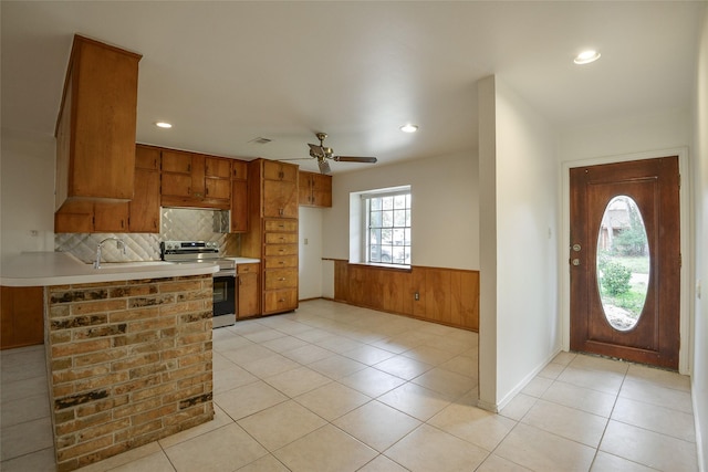 kitchen featuring kitchen peninsula, decorative backsplash, ceiling fan, sink, and stainless steel electric range