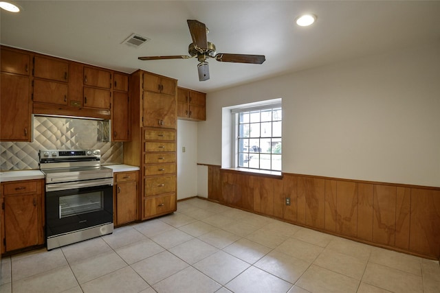 kitchen featuring stainless steel electric stove, ceiling fan, and wood walls