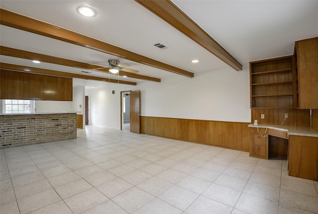 unfurnished living room with ceiling fan, beamed ceiling, and brick wall