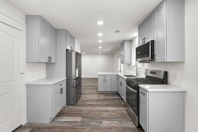 kitchen with sink, gray cabinets, light stone countertops, dark hardwood / wood-style flooring, and stainless steel appliances