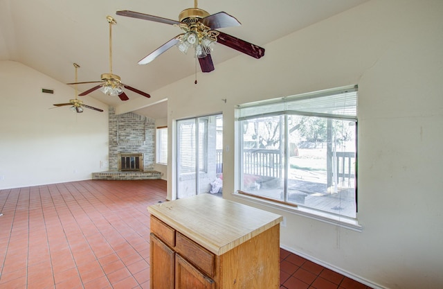 interior space featuring a center island, tile patterned floors, vaulted ceiling, ceiling fan, and a fireplace