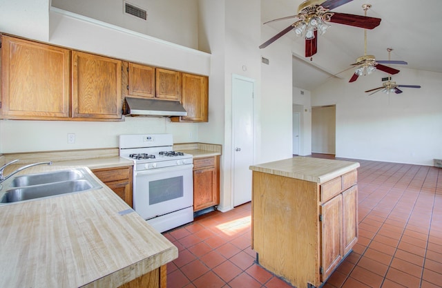 kitchen featuring white gas range oven, ceiling fan, sink, dark tile patterned flooring, and a kitchen island