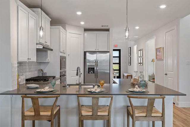 kitchen with sink, a kitchen breakfast bar, pendant lighting, white cabinets, and appliances with stainless steel finishes