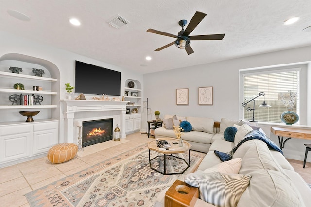 living room featuring built in shelves, ceiling fan, light tile patterned flooring, and a textured ceiling