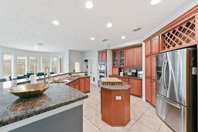 kitchen featuring a kitchen island with sink, dark stone counters, sink, light tile patterned floors, and stainless steel appliances