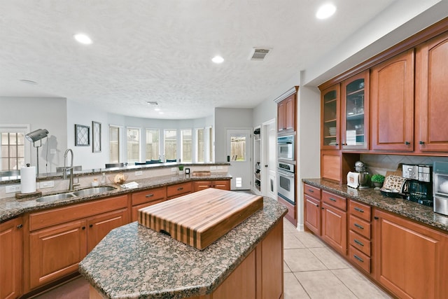 kitchen featuring oven, sink, light tile patterned floors, a textured ceiling, and a kitchen island