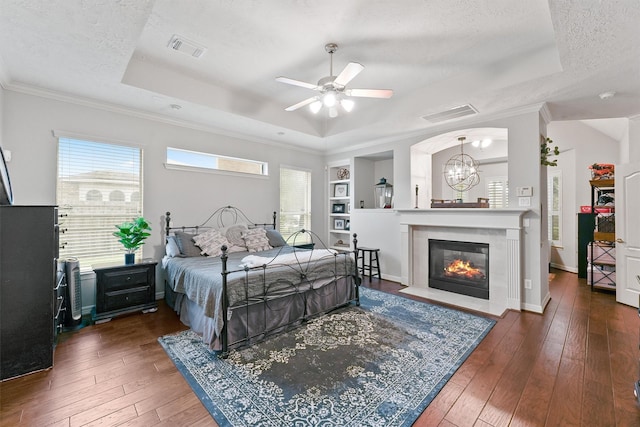 bedroom featuring ceiling fan with notable chandelier, dark hardwood / wood-style flooring, a raised ceiling, and a textured ceiling