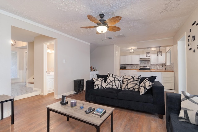 living room featuring sink, ceiling fan, light wood-type flooring, a textured ceiling, and ornamental molding