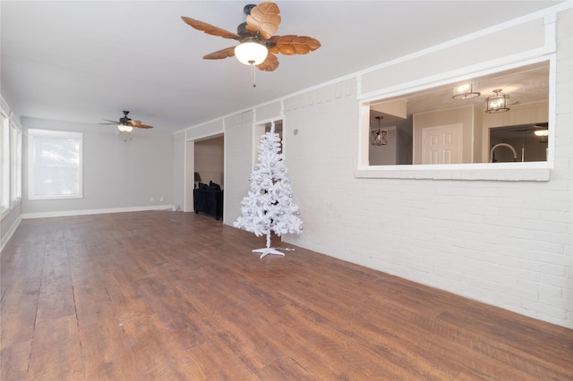 unfurnished living room featuring hardwood / wood-style floors, ceiling fan, and brick wall