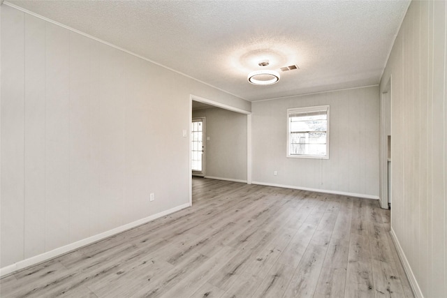 spare room featuring wood walls, light wood-type flooring, and a textured ceiling