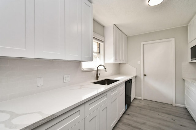 kitchen featuring white cabinets, black dishwasher, light stone countertops, and sink