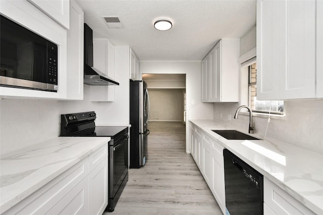 kitchen with white cabinets, light stone counters, wall chimney exhaust hood, and black appliances