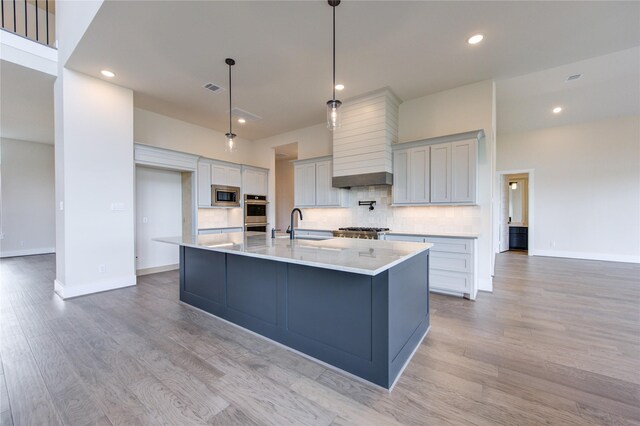 kitchen with a large island, hanging light fixtures, stainless steel appliances, tasteful backsplash, and light hardwood / wood-style floors