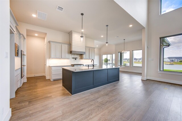 kitchen with decorative light fixtures, light hardwood / wood-style floors, white cabinetry, and a large island with sink