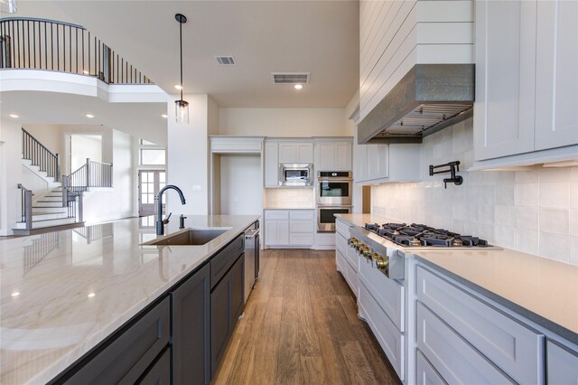 kitchen with white cabinets, sink, appliances with stainless steel finishes, decorative light fixtures, and custom range hood