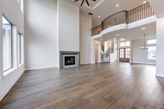 unfurnished living room featuring ceiling fan with notable chandelier, dark wood-type flooring, a high ceiling, and french doors