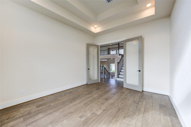 empty room featuring light hardwood / wood-style floors, french doors, and a tray ceiling