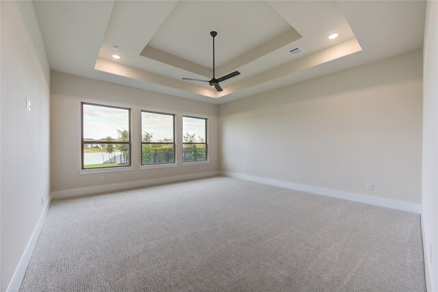 carpeted empty room with a raised ceiling and ceiling fan