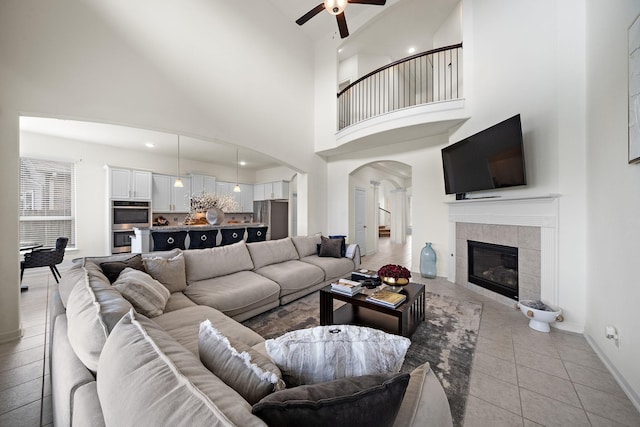 tiled living room with a tile fireplace, a high ceiling, and ceiling fan