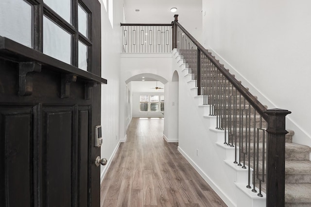 entrance foyer featuring wood finished floors, baseboards, arched walkways, ceiling fan, and a towering ceiling