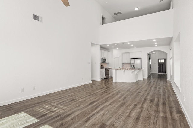 unfurnished living room featuring ceiling fan, dark wood-type flooring, and a high ceiling