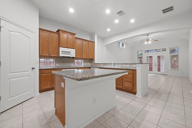 kitchen featuring light tile patterned flooring, ceiling fan, light stone countertops, a kitchen island, and kitchen peninsula