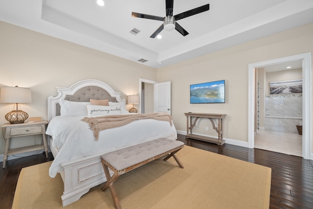 bedroom with ceiling fan, dark hardwood / wood-style floors, ensuite bathroom, and a tray ceiling