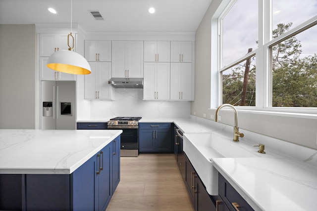 kitchen with blue cabinetry, white cabinetry, light stone countertops, decorative light fixtures, and appliances with stainless steel finishes