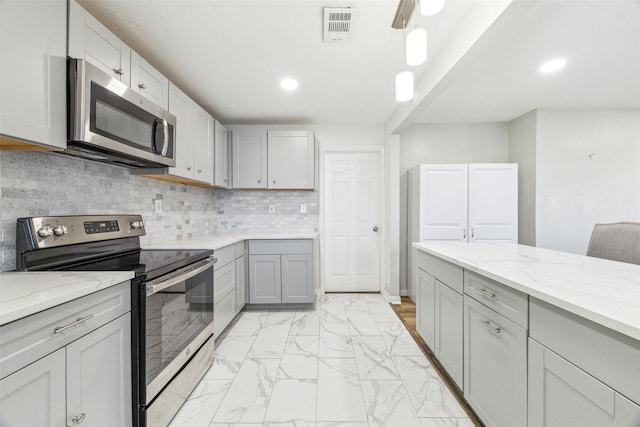 kitchen with gray cabinetry, light stone countertops, ceiling fan, backsplash, and appliances with stainless steel finishes