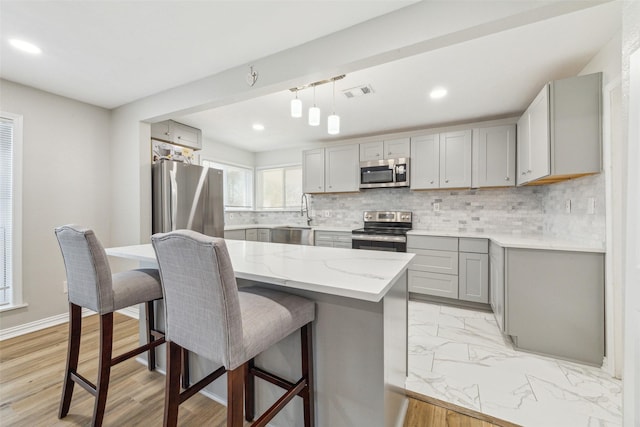 kitchen featuring light stone countertops, stainless steel appliances, a center island, gray cabinets, and hanging light fixtures