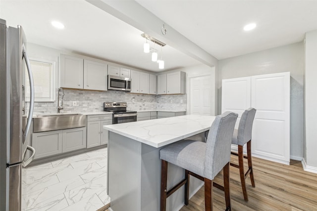 kitchen featuring light stone counters, stainless steel appliances, gray cabinets, and sink