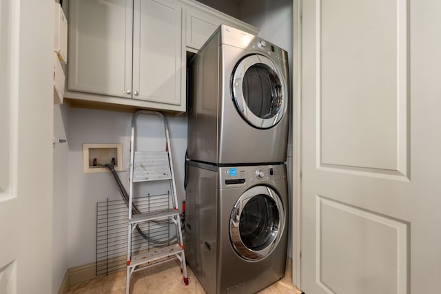 clothes washing area with cabinets, light tile patterned floors, and stacked washer and dryer