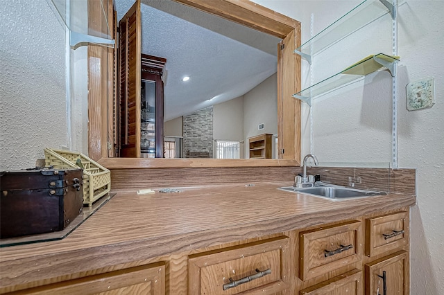 kitchen with a textured ceiling, sink, and lofted ceiling